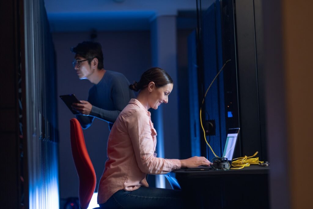 Caucasian female engineer using laptop and asian male engineer inspecting in computer server room