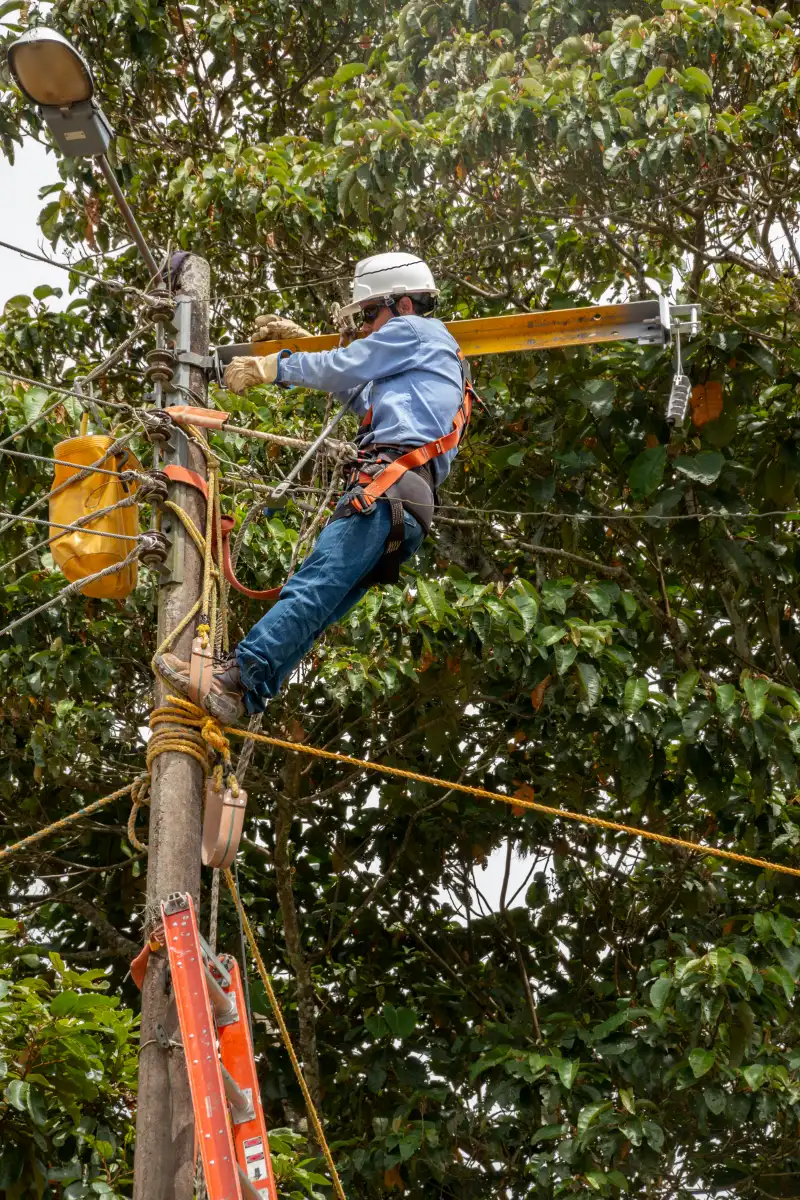 Emergencias Eléctricas en Medellín Operario en poste de luz repara líneas energizadas; trabajo en altura con equipo de seguridad para emergencias eléctricas